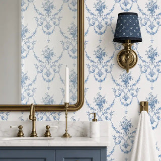 The Blue Garland wallpaper in Powder Blue & White installed on a feature wall in a bathroom behind a marble vanity with brass fixtures and a wall sconce. view-bathroom