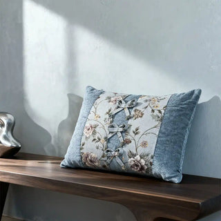 The Eternal Garden Blue Bow lumbar cushion styled on a dark wood designer bench in soft sunlight.