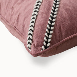 Close-up of the blush velvet cushion corner showing the braided black and white trim