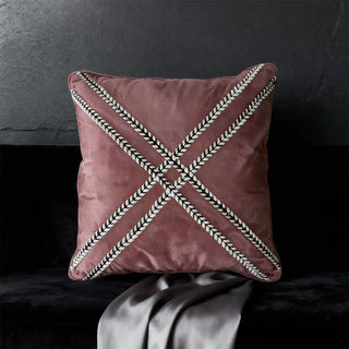 single blush cushion with cross braiding styled on a dark, plush sofa