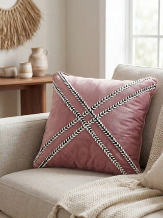 A luxury living room featuring the Blush Cross Braided cushion on a beige linen sofa with artisanal decor in the background.