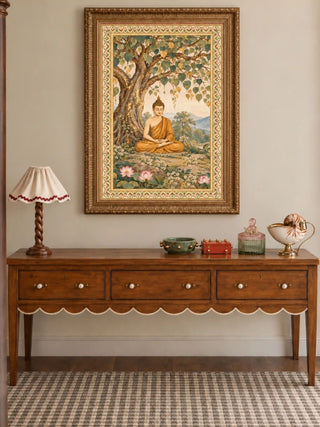 Bodhi Serenity wall art in an ornate antique-gold frame above a walnut console table with three drawers, a scalloped apron and a ruffled lamp