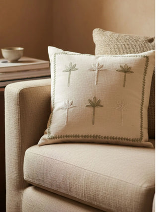 The Botanical Stitch cushion styled on a textured beige armchair in a bright, modern living room.