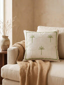 A luxury living room setting featuring the Botanical Stitch embroidered cushion on a cream sofa with a tan knit throw.