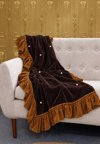 The Caramel Truffle sofa throw draped over a tufted cream sofa against gold art deco wallpaper.