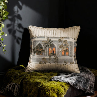 The Cattitude Courtyard cushion styled in a moody, dark setting with a green throw, highlighting the warm window accents.