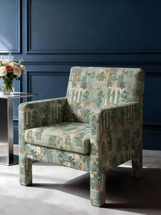 A modern square armchair upholstered in Cattitude teal fabric featuring cats and classical pillars against a dark blue wall.