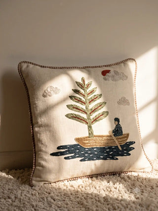 The Celestial Veil hand-embroidered linen cushion cover highlighting a fairytale pine tree boat styled on a textured rug in a sunlit lounge.