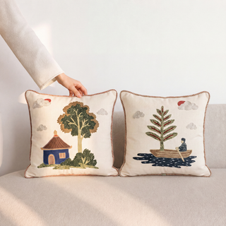 Hand-embroidered Celestial Village cushion covers styled on a cream boucle sofa in a warm, sunlit living room.