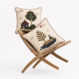 Celestial Village Pine and Pagoda cushion covers on a rattan folding chair, embroidered village scenes on ivory