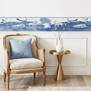 Chandni Van blue and white scenic wallpaper border installed above white paneling in a sitting area.
