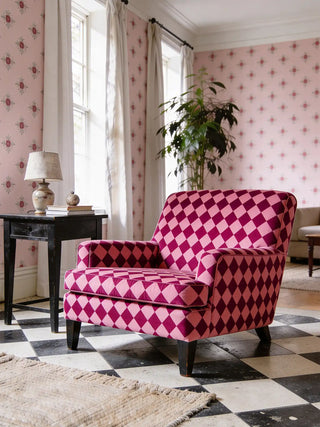 A luxury armchair upholstered in Chausar fabric featuring a magenta and rose diamond pattern set against a pink floral wallpaper.