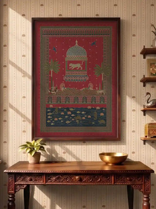 Chitrakar Pichwai wall art in madder red, framed in dark rosewood above a carved wooden console with a brass bowl and potted plant in a lotus-papered entryway.