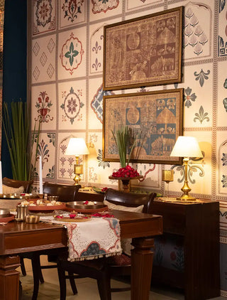 The Chitrangan wallpaper in a tiled grid of floral rosettes, arched niches and leaf sprays, behind a wooden dining table and console. view-dining