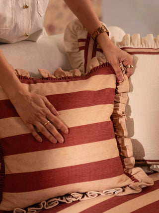 The Cinnamon Ruffle cushion cover in wide rust and peach stripes with a gathered peach ruffle edge, styled on a cream sofa.