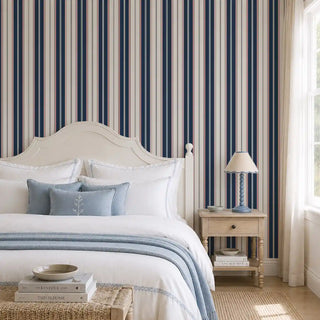 Classic Navy Pinstripe wallpaper behind a cream headboard and wooden nightstand in a bedroom.