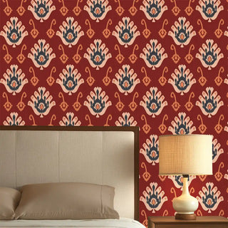 A red wallpaper featuring traditional nomadic-inspired motifs in beige and blue tones, styled behind a bed with a bedside lamp.