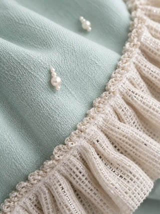 A close-up of the Cloudveil sofa throw showing a pearl bead cluster and the open-weave ivory ruffle.