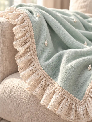 A close-up of the Cloudveil sofa throw's gathered ivory ruffle border with pearl clusters on the seafoam body.