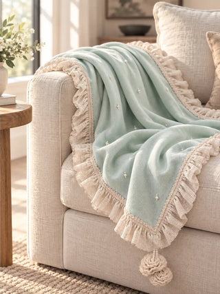 The Cloudveil sofa throw in Seafoam & Ivory draped over a sofa arm beside a wooden side table in soft window light.