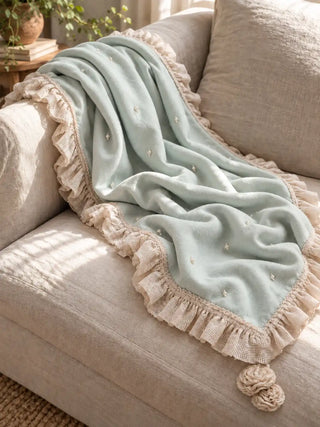 The Cloudveil sofa throw in Seafoam & Ivory draped over a linen sofa, showing the ruffled ivory border and rosette drops.