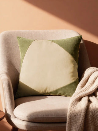 A luxury Corner Caps cushion cover in sage green and cream velvet featuring a modern geometric design on a beige armchair.