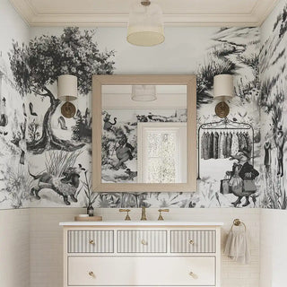 A black and white wallpaper featuring an artistic countryside animal scene with people, trees, and rustic elements, applied in a pwder room setting with a vanity mirror and lights.
