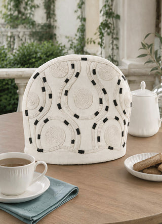 The Cozy Trace tea cosy in Ivory, view-outdoor styled on a terrace table with tea and biscuits.