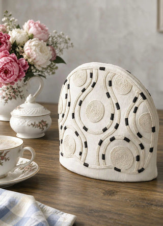 The Cozy Trace tea cosy in Ivory, view-tablesetting beside peonies and a bone china teacup.