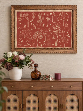 The Crimson Garden wall art print, framed in carved wood and displayed above a console styled with a vase of flowers, a glass decanter and a candle.