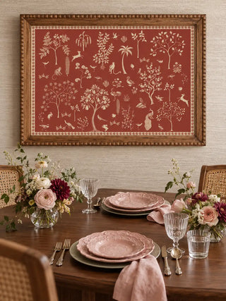 The Crimson Garden wall art print, framed in carved wood, displayed above a dining table set with floral centrepieces and pink china.