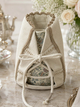 Front view of Deep Lore jug cover in cream waffle weave showing cotton cord bow lacing and ceramic floral jug inside.