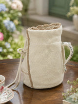 Side profile view of Deep Lore jug cover fitted around a ceramic jug handle on a wooden garden tea table.