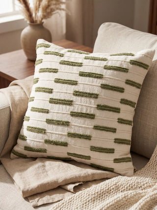 A close-up of a luxury cream cushion featuring a hand-embroidered sage green palm tree on a soft neutral sofa.