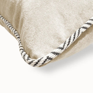 Close-up of the beige velvet cushion corner showing the braided black and white piping.