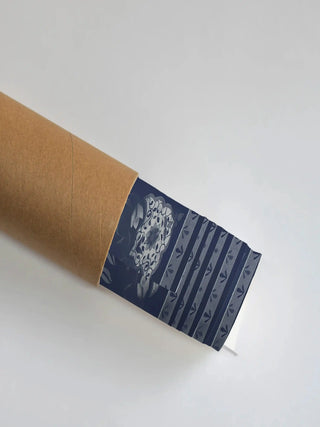 The Dilli Darbar wall art print in indigo blue, partially unrolled from its kraft paper shipping tube, showing a floral medallion and striped sprig border.