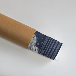 The Dilli Darbar wall art print in Navy & Powder Blue, partially unrolled from its kraft paper shipping tube, showing an ornamental medallion with trailing vine beside a striped leaf-sprig panel.