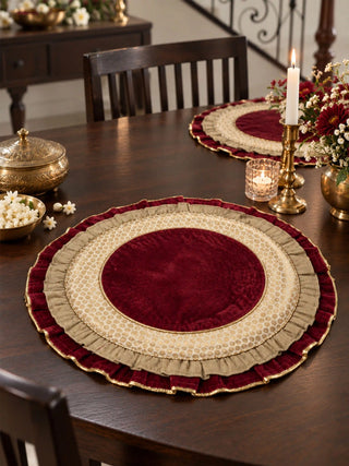Diyaara round crimson velvet table mat set styled on a polished dark wood dining table with brass candelabras and brass bowls.