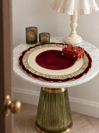 Diyaara round velvet mat displayed on a white marble side table with a red decorative box, table lamp, and votive candles.