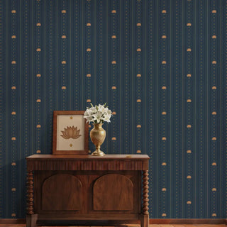 The Doriya deep blue pinstriped wallpaper styled in a foyer behind a dark carved wooden console table with a brass flower vase.