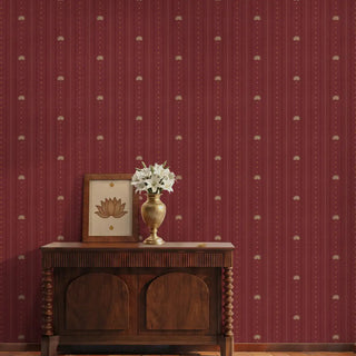 The Doriya rich red pinstriped wallpaper styled in a foyer behind a dark carved wooden console table with a brass flower vase.