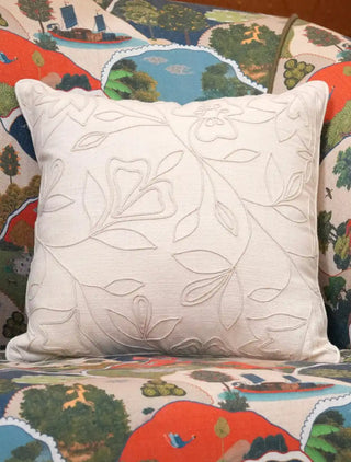 The Eden cushion cover in ivory with raised tonal leaf, flower and vine outlines and matching piping, styled on a scenic printed sofa.