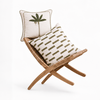 The Eka Kanan & Ari Garden cushion cover gift set styled on a woven rattan bench, showing an olive-green embroidered banana leaf tree cushion and a tufted dash-stripe cushion, both on natural cotton-linen.