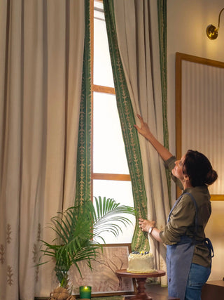 The Elfdale curtain in beige with a green leaf-sprig border and tan leaf motifs at the hem, hung at a tall wooden window.