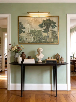 Neoclassical garden wall art displayed above a dark wood console table with a bust and fresh flowers in a sage green foyer.