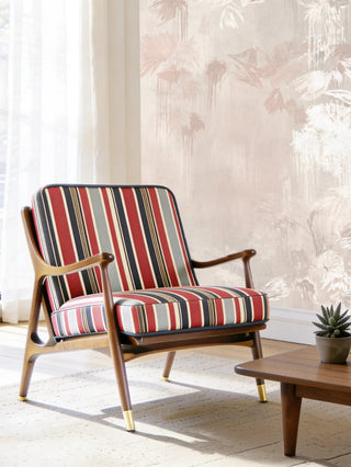 A luxury mid-century modern armchair upholstered in English Style Stripes red and blue fabric against a soft floral mural.