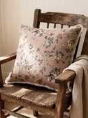 A luxury Eternal Garden cushion in dusty rose featuring vintage floral tapestry and a fringed border on an antique wooden chair.