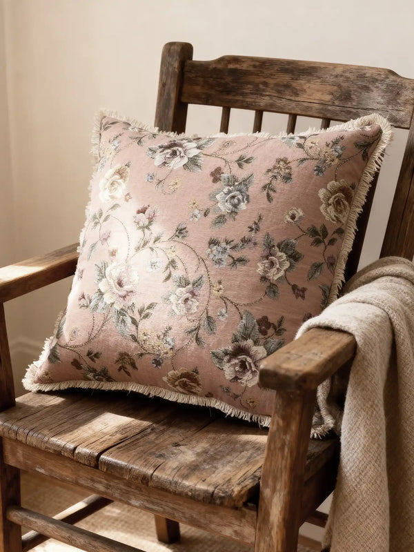 A luxury Eternal Garden cushion in dusty rose featuring vintage floral tapestry and a fringed border on an antique wooden chair.