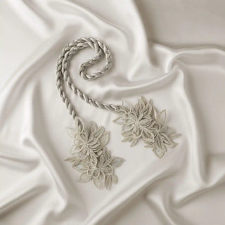 Flat lay of the Ethereal Petals Tieback, showcasing the silvery-gray braided cord and the detailed embroidered lace flower clusters.