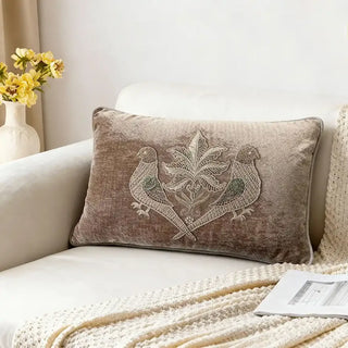 Taupe velvet cushion with parrot embroidery on white sofa.